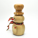 A handcrafted wooden snowman figurine with a natural light wood finish, featuring a plaid red, green, and white scarf, a small red nose, and silver decorative studs on the hat and body.