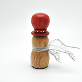 A handcrafted wooden snowman figurine with a reddish-brown top ball, a natural wood body, a red band with silver studs, and a sheer silver ribbon tied around its neck, set against a plain white background.