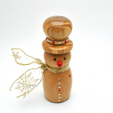 A wooden snowman figurine with a warm honey-toned wood finish, featuring a red nose, silver and red buttons, a gold glitter neckband with rhinestones, and a gold ribbon scarf with a printed snowflake design.