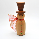 A wooden snowman decoration with a dark brown top hat, a light natural wood body, red and green decorative buttons, and a red glittery scarf, styled with warm fairy lights, gold beads, and holiday ornaments.