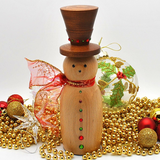 A wooden snowman decoration with a dark brown top hat, a light natural wood body, red and green decorative buttons, and a red glittery scarf, styled with warm fairy lights, gold beads, and holiday ornaments.